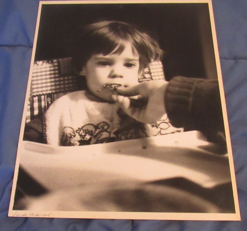 1977 Sandy Underwood photograph; child eating in high chair #2, 11″ x 14″