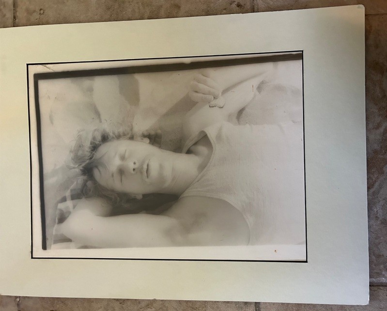 black and white photograph of Paul Thek in undershirt lying down eating an Orio